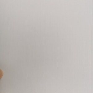 May include: A close-up of a white, textured paper with a subtle grid pattern. The paper is held by a hand, and the background features a white and gray tiled surface.
