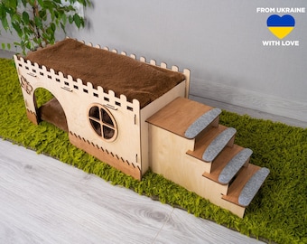 May include: Wooden cat house with a brown plush bed on top, a small window, and a set of stairs with gray felt pads. The house is on a green rug with the text "FROM UKRAINE WITH LOVE" and a yellow and blue heart.