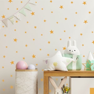 Peut inclure: Un ensemble d'autocollants muraux composé de nombreuses étoiles jaune moutarde de tailles variées dispersées sur une surface unie. Les étoiles sont disposées selon un motif créant un effet céleste, offrant un élément décoratif simple et répétitif.