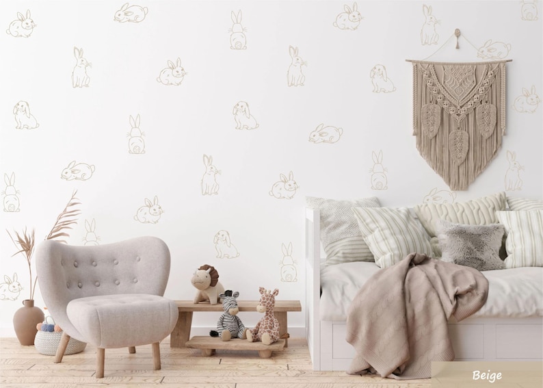 K&ouml;nnte beinhalten: Eine Wand mit einem sich wiederholenden Muster aus beigen Linien-Hasen-Aufklebern. Die Hasen sind in verschiedenen Posen dargestellt, darunter sitzend, liegend und stehend. Die Wand ist Teil eines Raumes mit einem hellen Sessel, einer Holzbank mit Pl&uuml;schtieren und einem Tagesbett mit Kissen und einem Makramee-Wandbehang.