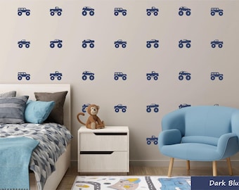 May include: A white wall with a repeating pattern of dark blue monster truck decals. The wall is in a room with a blue armchair and a white nightstand.