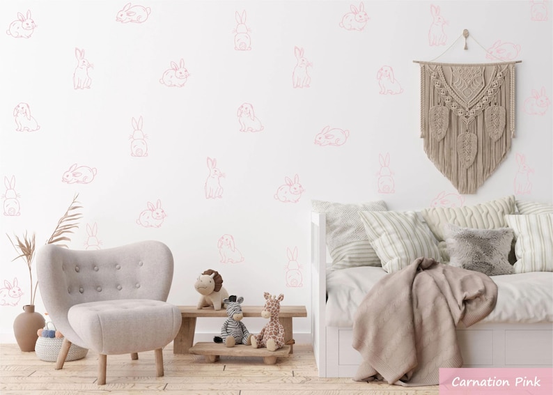 K&ouml;nnte beinhalten: Ein Set aus nelkenrosa Wandaufklebern in Hasenform, die in verschiedenen Posen &uuml;ber eine wei&szlig;e Wand verteilt sind. Die Wandsticker bestehen aus einfachen Strichzeichnungen von Hasen in unterschiedlichen Positionen, darunter sitzend, liegend und stehend.