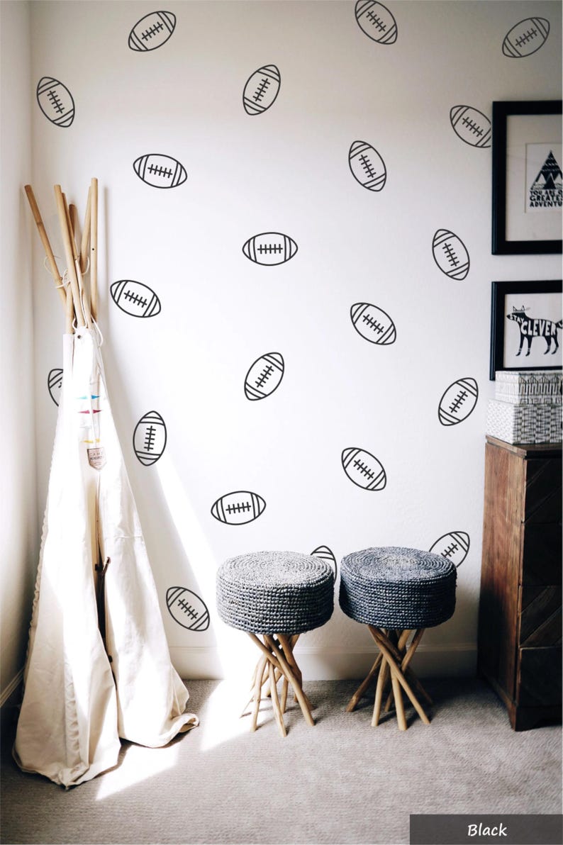 May include: A set of black American football wall decals featuring a simple line art design of a rugby-style ball. These individual stickers are arranged in a scattered pattern across a white wall, providing a decorative accent for a room.