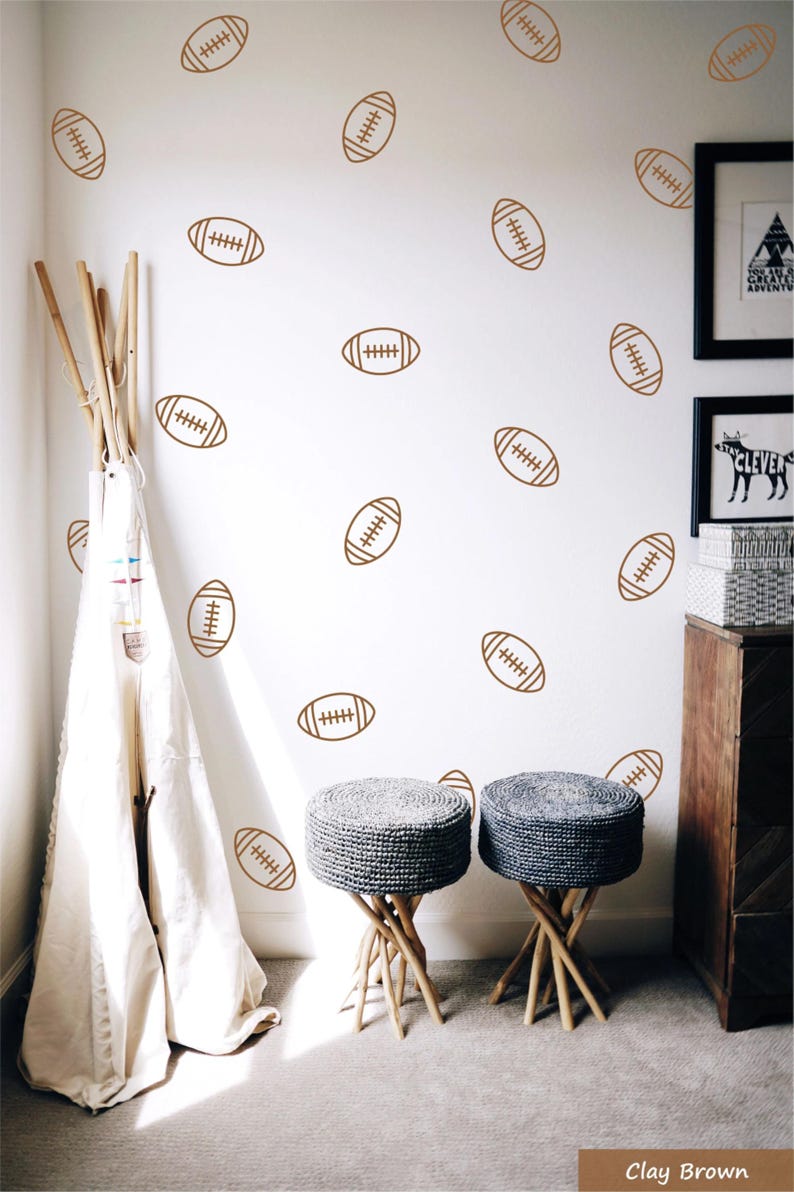 May include: A set of wall decals featuring a repeating pattern of brown American football outlines. The decals are applied to a white wall, creating a decorative motif of various footballs oriented in different directions across the surface.