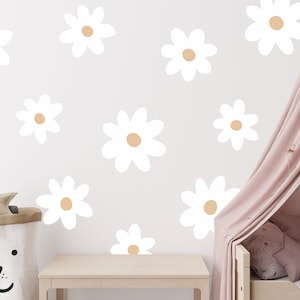 May include: White daisy wall decals with a light brown centre, arranged on a white wall. A pink canopy bed with pillows is in the background.