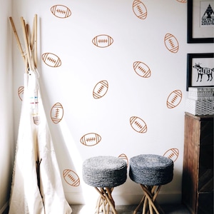 May include: A set of wall decals featuring a repeating pattern of brown American footballs. The footballs are illustrated with simple line art showing the laces and stitching. These decals are applied to a plain white wall surface.