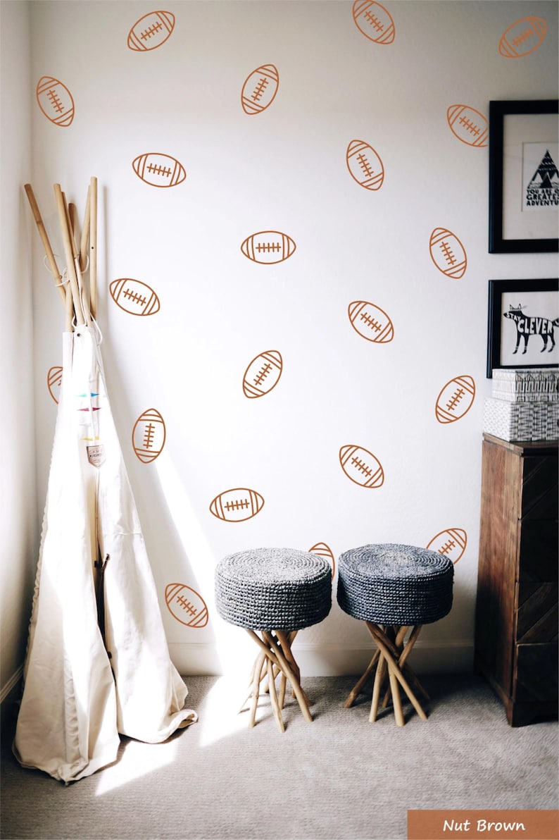 May include: A set of wall decals featuring a repeating pattern of brown American footballs. The footballs are illustrated with simple line art showing the laces and stitching. These decals are applied to a plain white wall surface.