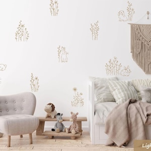 May include: A light brown nursery with a white wall featuring a wall decal of a bunny and flowers. The room has a white sofa with a light brown blanket, a light brown armchair, and a wooden table with a stuffed giraffe and zebra.