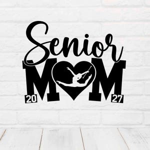 May include: Black graphic design featuring the words "Senior Mom" with a heart-shaped center. Inside the heart is a silhouette of a baton twirler. The numbers "20" and "27" are on either side of the "M".