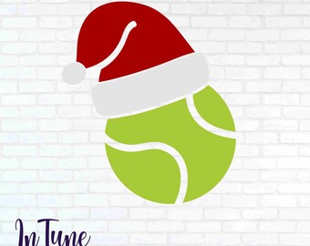 May include: A green tennis ball with white curved lines, wearing a red Santa hat with a white trim and pom-pom. The image is set against a white brick wall background. The text "In Tune DIGITAL DESIGNS" is at the bottom.