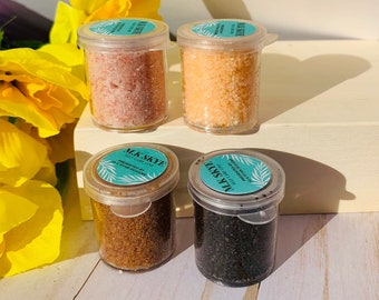 Può includere: Quattro piccoli barattoli trasparenti pieni di sali da bagno colorati. I barattoli sono etichettati "M.K. Skye Self Care Line". I sali sono rosa, arancioni, marroni e neri. Fiori gialli sullo sfondo.