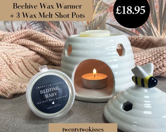 May include: A white ceramic beehive wax warmer with a lit candle inside, accompanied by three wax melt shot pots. The warmer has a decorative bee on the lid. The text on the wax melt pot reads "Bedtime Baby".
