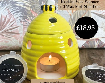 May include: A yellow ceramic beehive wax warmer with a white and black bee design on top. The warmer has hexagonal cutouts and a lit tea light inside. Includes three wax melt shot pots. The text "Beehive Wax Warmer + 3 Wax Melt Shot Pots" is visible.