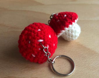 May include: Two crocheted mushroom keychains, one red with white spots and one white with a red top, attached to a silver key ring.