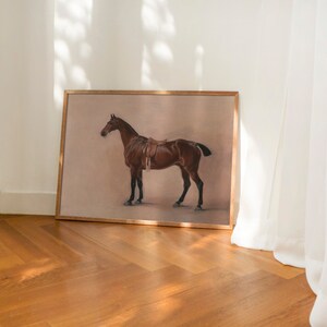 May include: A framed print of a brown horse with a saddle, standing on a light brown background.