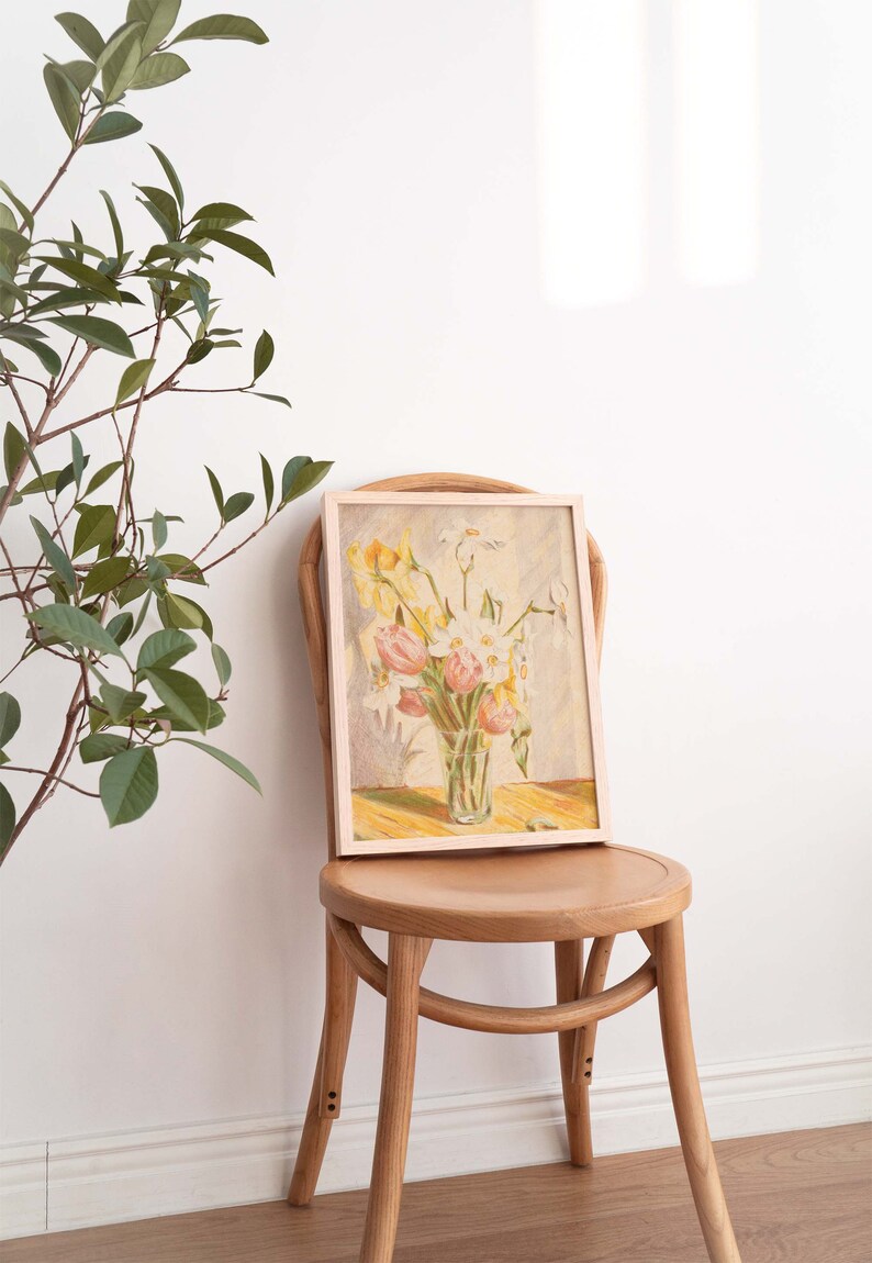 May include: A framed painting of a bouquet of yellow, white, and pink flowers in a glass vase. The painting is on a wooden chair with a light wood finish.