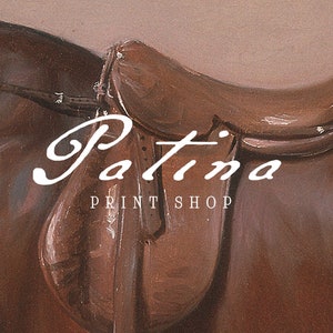 May include: A brown leather saddle with the text "Patina Print Shop" in white lettering.
