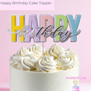 May include: A white iced cake with a colourful "HAPPY birthday" cake topper. The topper has pastel yellow, purple, pink, green, and blue letters. The word "birthday" is in a silver script font.