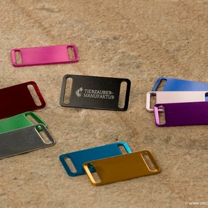 Könnte beinhalten: Sortiment an bunten Metall-Hundeanhängern mit einem schwarzen Anhänger, der mit "Tierzauber-Manufaktur" graviert ist.