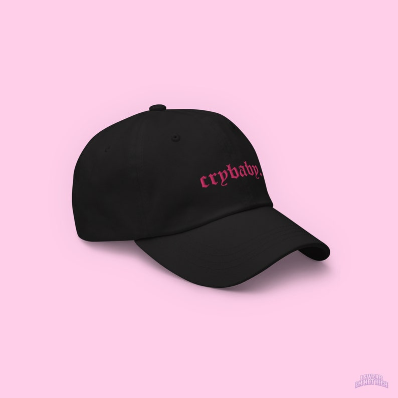 Puede incluir: Una gorra de b&eacute;isbol negra con un "crybaby" bordado en rosa en una fuente g&oacute;tica.