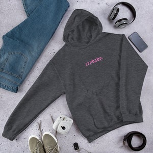 May include: A dark gray hooded sweatshirt with a pink embroidered design that says "crybaby."