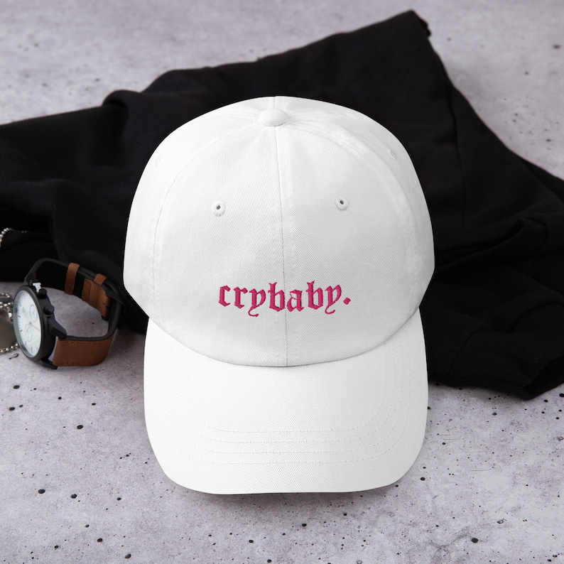 Puede incluir: Gorra de b&eacute;isbol blanca con un texto bordado en rosa que dice "crybaby."
