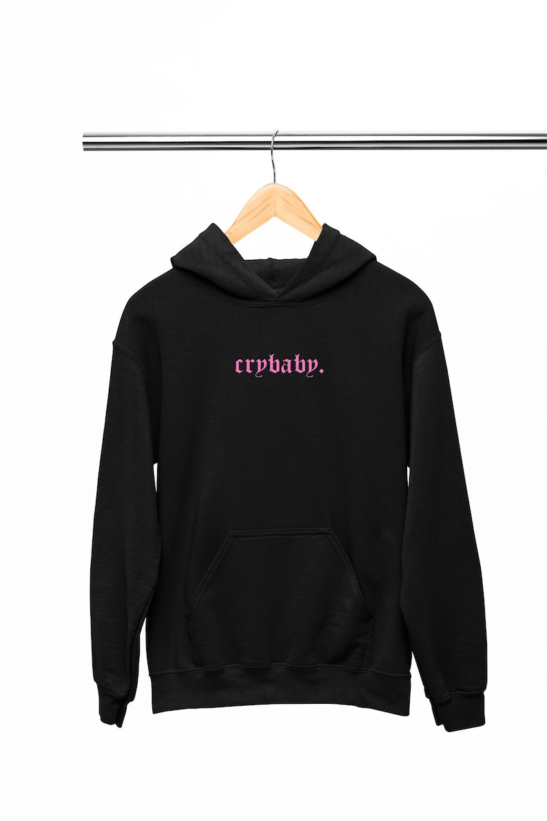 May include: Black hoodie with a pink "crybaby." graphic printed on the front.