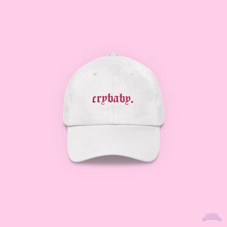 May include: White baseball cap with a pink embroidered text that says "crybaby."