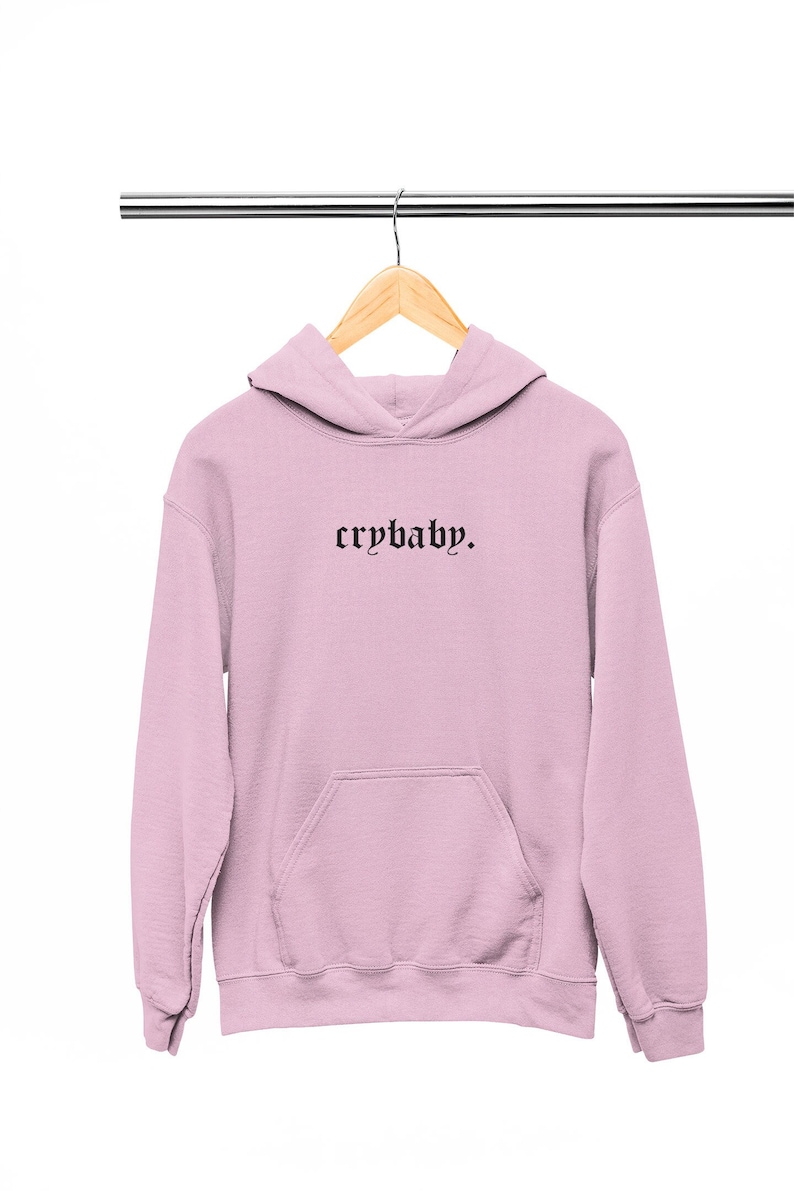 May include: A pale pink hoodie with black embroidered text that reads "crybaby."