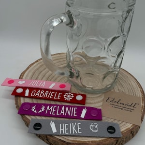 Op de afbeelding: Vier kleurrijke vilt drankmarkeringen met verschillende namen en ontwerpen. De namen zijn Julia, Gabriele, Melanie en Heike. De ontwerpen omvatten een hart, een reuzenrad, geweien en een bierpul.