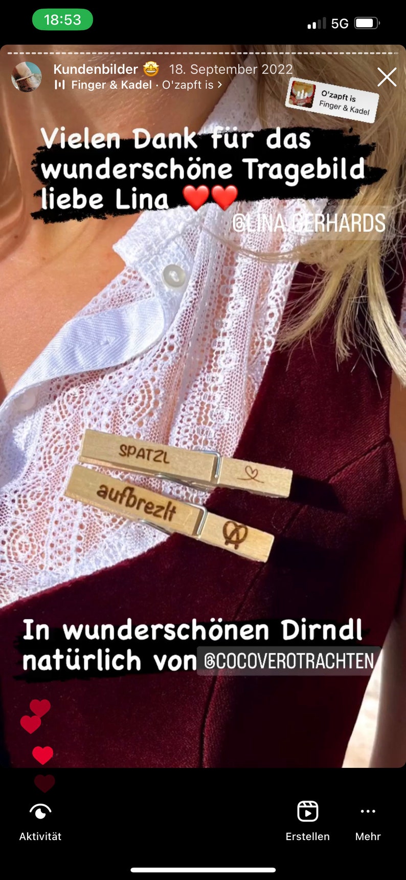 May include: Two wooden clothespins featuring engraved text and symbols. The top pin displays the word SPATZL with a heart icon, while the bottom pin features the word aufbrezlt and a pretzel icon. These items are attached to a dark red garment.