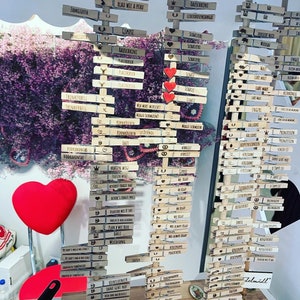 May include: Three vertical wooden displays holding numerous light-colored wooden clothespins, each engraved with German text and small icons like hearts, crowns, and pretzels. Three red heart-shaped cutouts are attached to the center display.