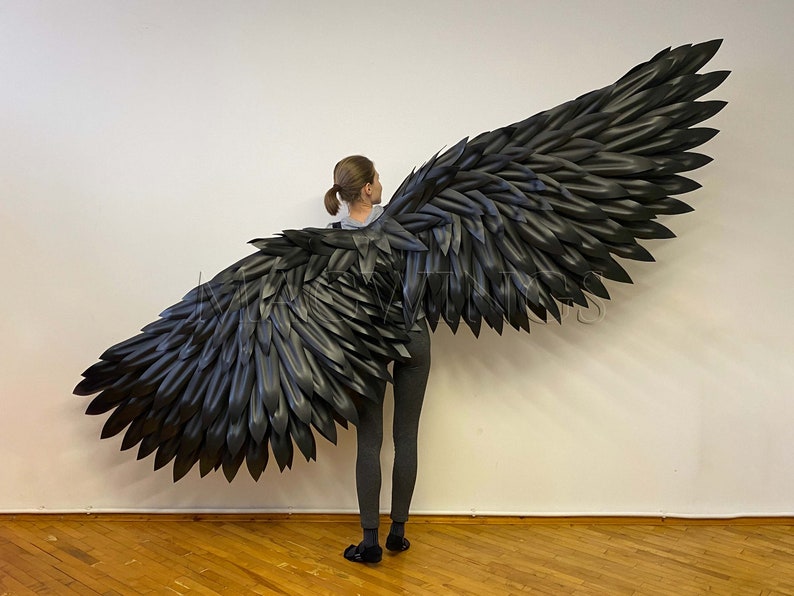 May include: A person wearing black clothing with large, black, feathered wings attached to their back. The wings are spread out behind them, creating a dramatic effect.