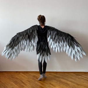 May include: A pair of large, black and white feathered wings. The wings are made of individual feathers that are attached to a base. The wings are spread out and are being held by a person.