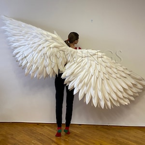May include: A person wearing white angel wings made of feathers. The wings are large and cover the person's back. The wings are white and have a feathery texture.