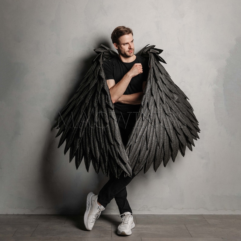 May include: A person wearing a black shirt and black angel wings. The wings are large and feathery, and the person is looking to the side.