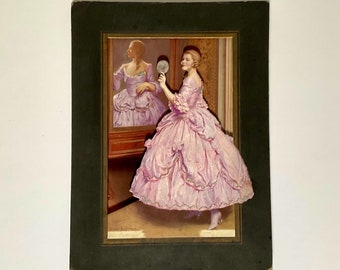 May include: A framed vintage print of a woman in a pink gown holding a hand mirror. The woman is looking at her reflection in the mirror. The print is in a dark green frame.