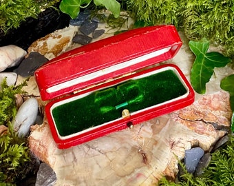 May include: A red velvet ring box with a green velvet interior. The box is open and the lid is propped up.