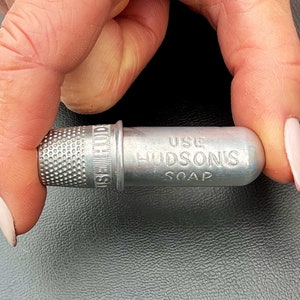 May include: A silver thimble attached to a small metal container with the text "USE HUDSON'S SOAP" engraved on it.