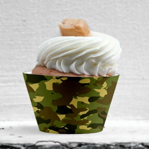 May include: Green, brown and yellow camouflage cupcake wrapper. The wrapper is made of paper and has a printed design. The cupcake is topped with white frosting and a brown peanut butter topping.