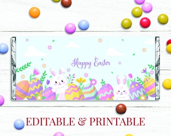 May include: Printable Easter chocolate bar wrapper featuring two white bunnies with pink noses and ears, surrounded by colorful Easter eggs and flowers. The wrapper has a light blue background with white clouds and the text "Happy Easter".