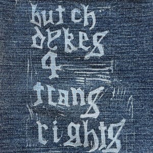 May include: Close-up of blue denim fabric with white text in a gothic font. The text reads "butch dekes 4 ftang rights". The fabric has a worn appearance with visible stitching and faded areas.
