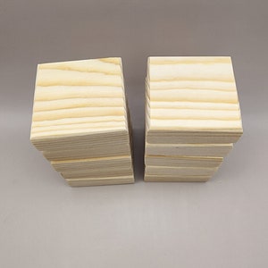 K&ouml;nnte beinhalten: Zwei Stapel quadratischer Holzbl&ouml;cke, die jeweils eine hellbraune Farbe mit sichtbaren nat&uuml;rlichen Holzmaserungsmustern aufweisen, die horizontal &uuml;ber die Oberfl&auml;chen verlaufen. Die Bl&ouml;cke sind in zwei separaten, vertikalen S&auml;ulen angeordnet.