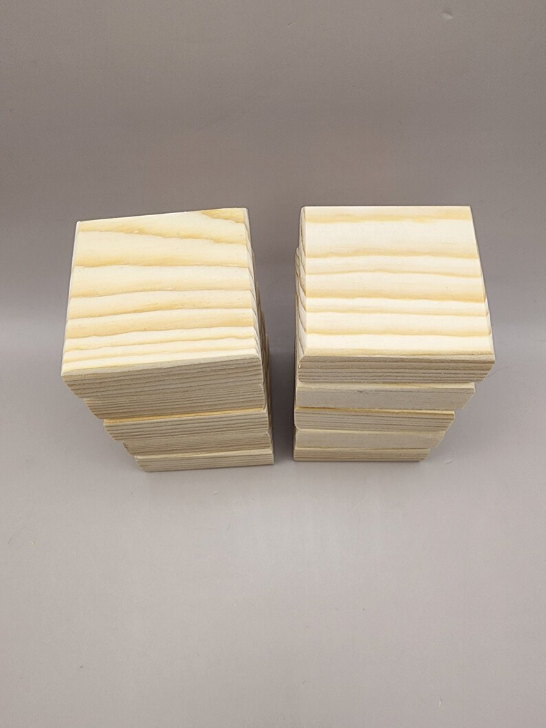 K&ouml;nnte beinhalten: Zwei Stapel quadratischer Holzbl&ouml;cke, die jeweils eine hellbraune Farbe mit sichtbaren nat&uuml;rlichen Holzmaserungsmustern aufweisen, die horizontal &uuml;ber die Oberfl&auml;chen verlaufen. Die Bl&ouml;cke sind in zwei separaten, vertikalen S&auml;ulen angeordnet.