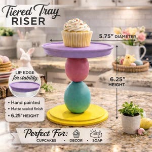 May include: A hand-painted, matte-finished tiered tray riser. The riser is 6.25 inches tall and features a yellow base, a teal mid-section, a pink center, and a purple top. The top has a 5.75-inch diameter and holds a cupcake. The text reads "Tiered Tray Riser".