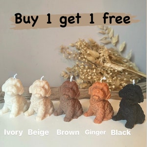 May include: Five small dog-shaped candles in ivory, beige, brown, ginger, and black. The candles are arranged in a row on a wooden surface. The text "Buy 1 get 1 free" is displayed above the candles.
