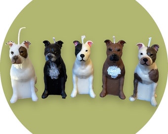 May include: Five white, black, and brown dog candles. The candles are all sitting upright on a green background.