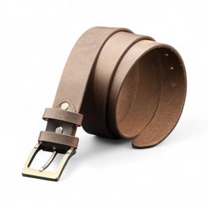 May include: A rolled-up brown leather belt with a rectangular brass buckle. The belt is a medium brown color and appears to be made of high-quality leather. The buckle is a classic design, with a single prong.