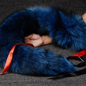 May include: A blue fox fur tail with red ribbon accents. The tail is curled into a circle shape.