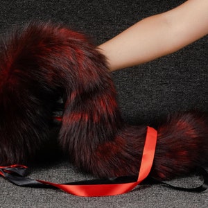 Può includere: Una coda di pelliccia finta rossa e nera con un nastro rosso legato intorno. La coda è sdraiata su una superficie grigia.